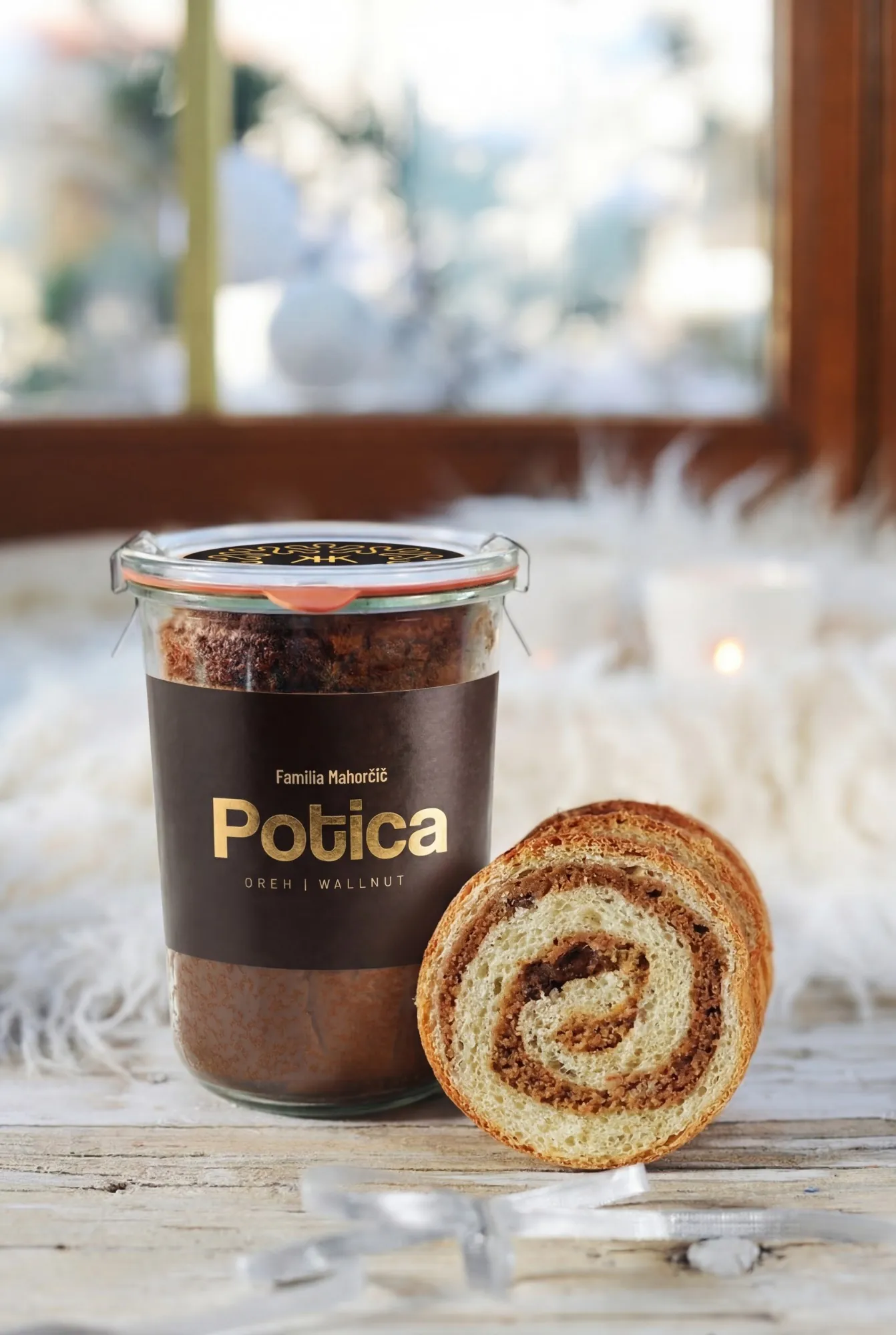 Potica in vasetto con l’etichetta Familia Mahorčič e una fetta di potica alle noci davanti a una finestra d’inverno